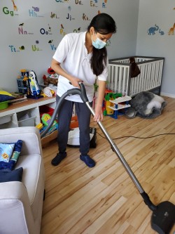 A person wearing a mask vacuums the hardwood floor of a child's playroom, which features toys, a crib, and alphabet decals on the wall, reflecting the care provided by cleaners Vancouver.